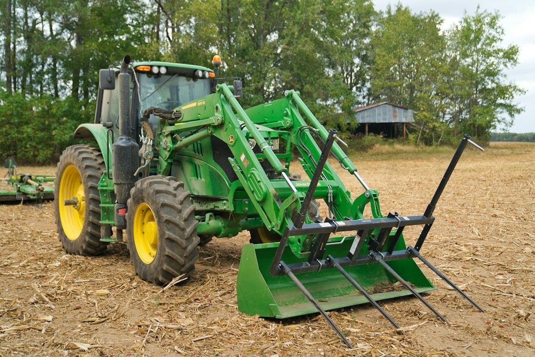 Grön traktor med frontlastare och redskap på ett skördefält